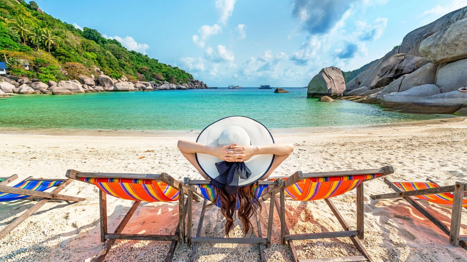 Woman with hat sitting on chairs beach in beautiful tropical bea