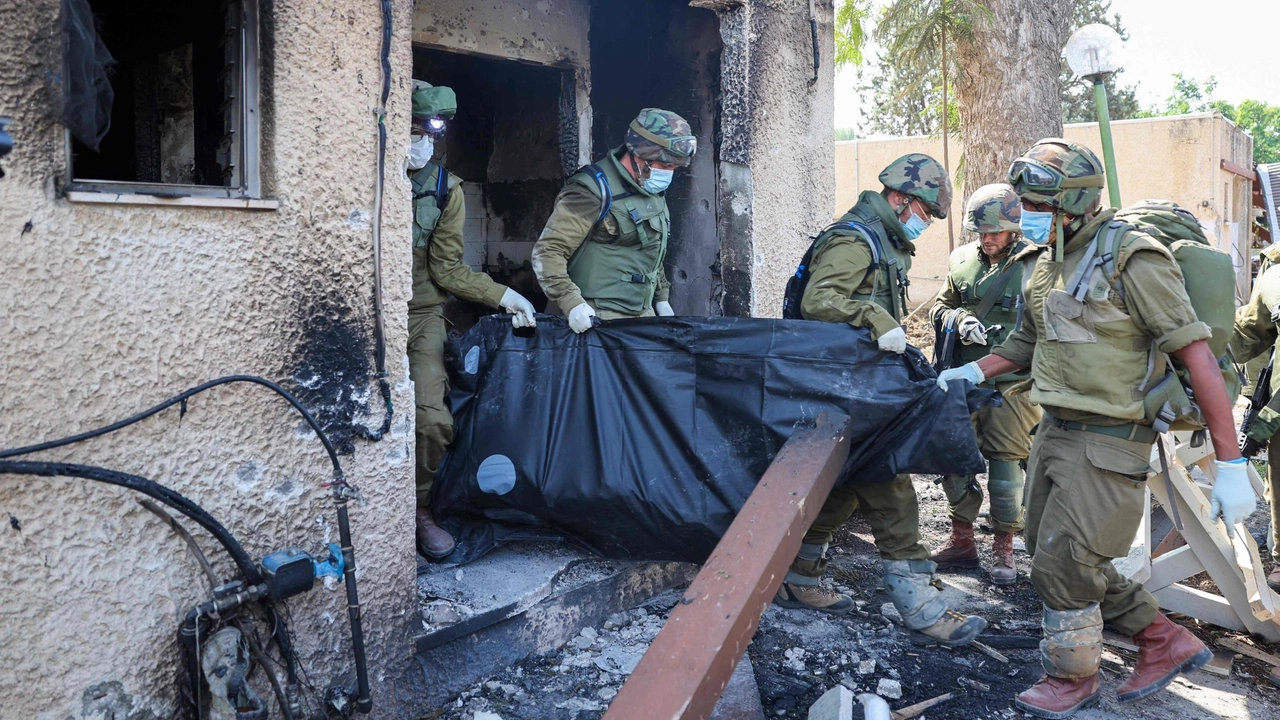 Soldati israeliani portano via corpi di israeliani uccisi nel kibbutz di Kfar Aza (Afp)