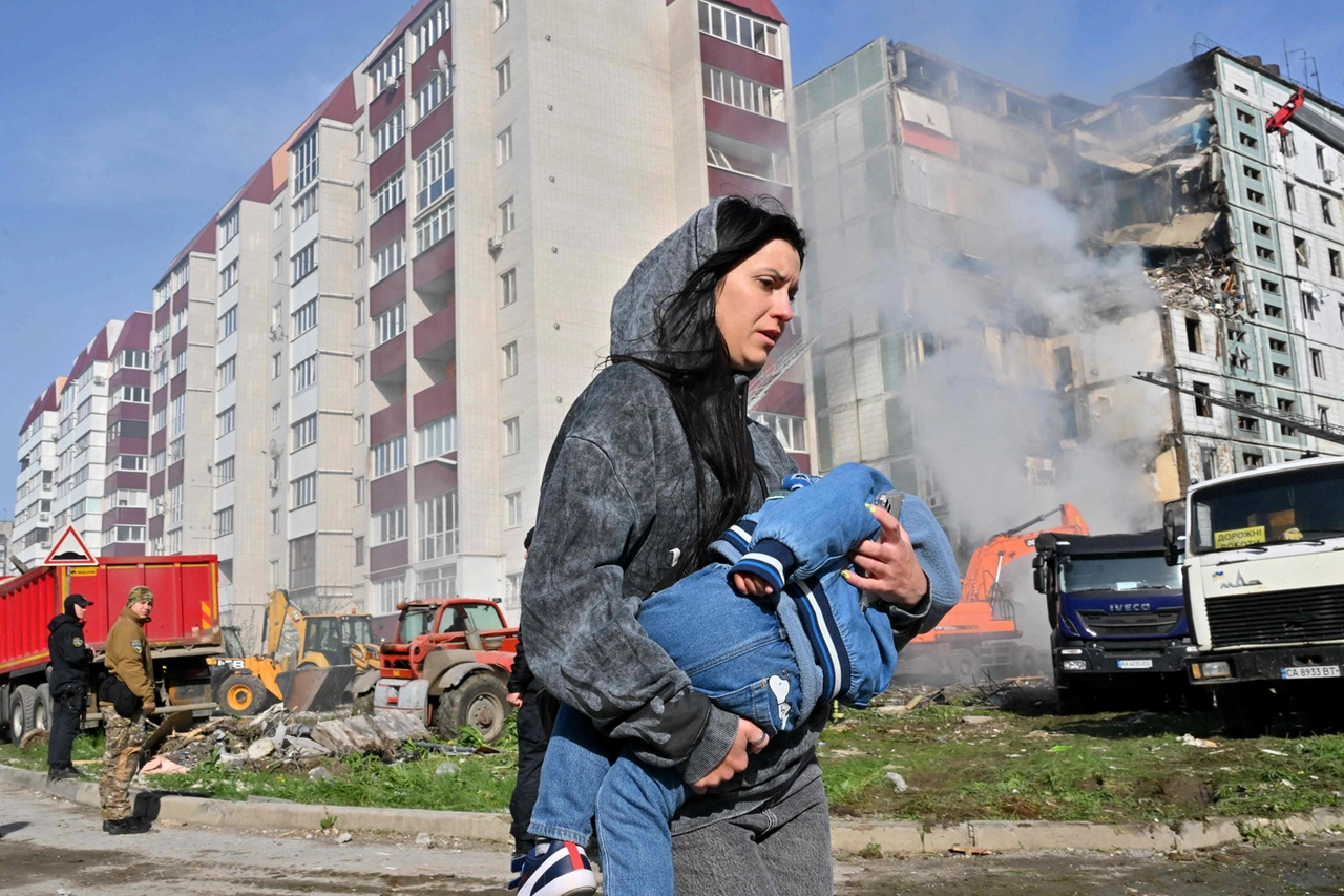 Un donna con in braccio un bambino davanti al condominio bombardato a Uman (Afp)