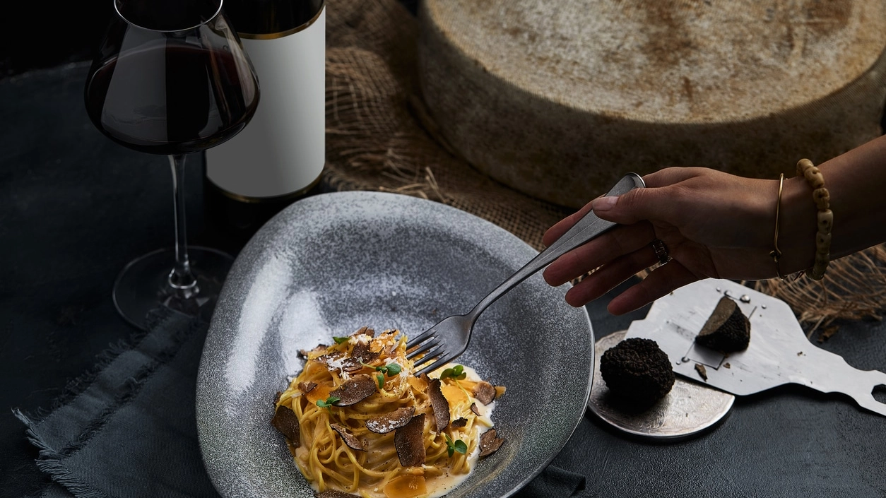 Italian cuisine - spaghetti with black truffle on a gray plate and bottle of wine. Selective focus. Vertical