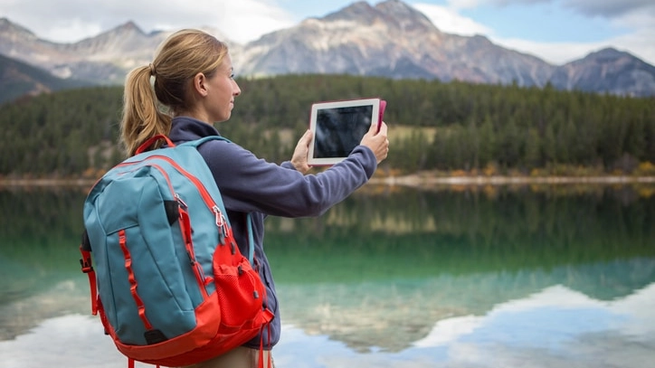 Woman hiking by the lake takes picture using digital tablet