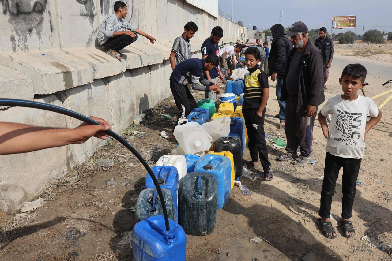 Palestinesi riempiono taniche d'acqua al valico di Rafah (Ansa)