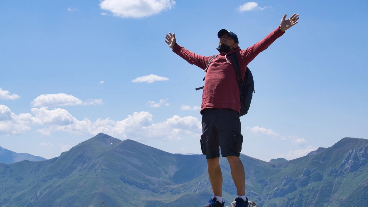 A white adult male on top of a mountain with his arms up in the air.