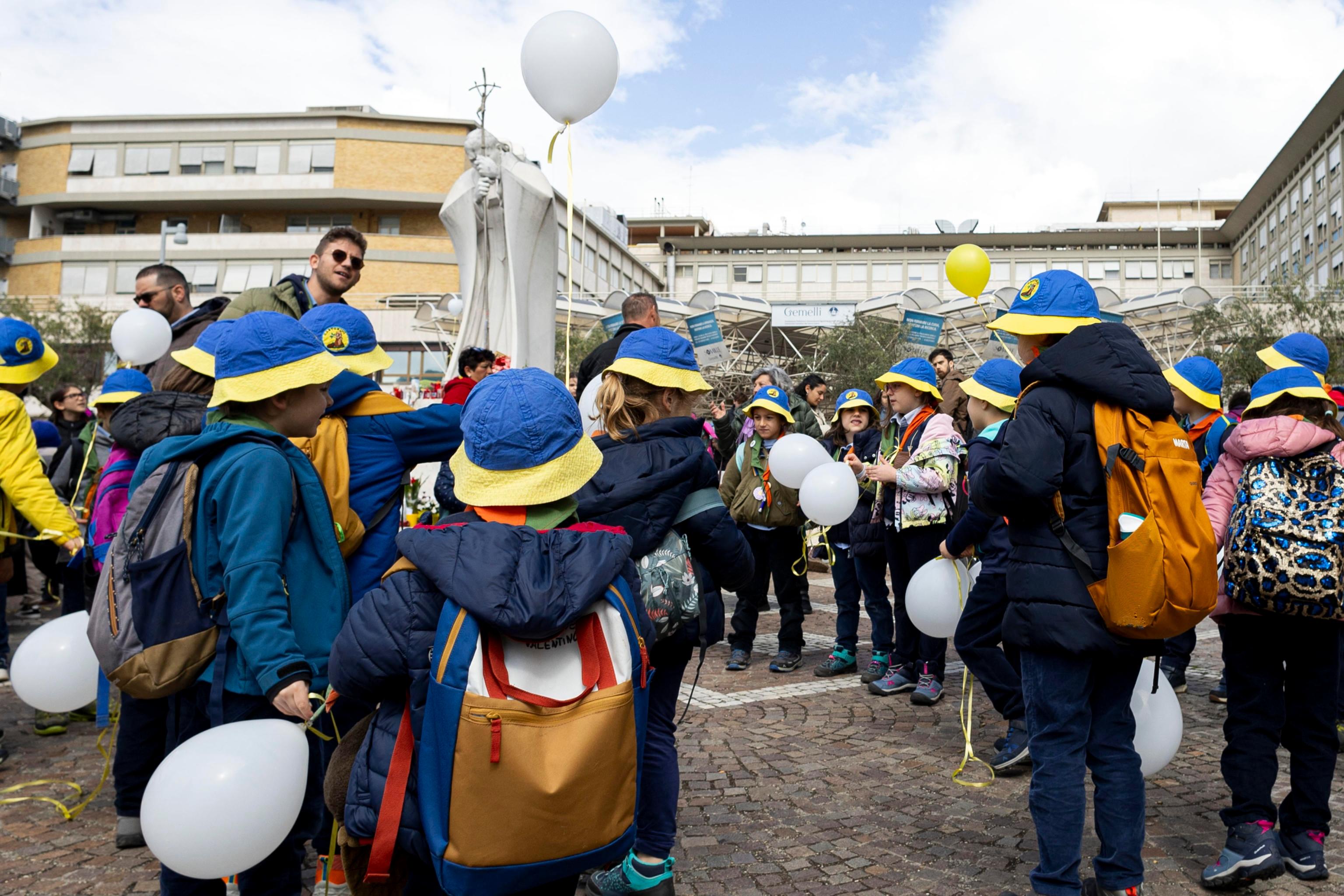 Un gruppo di bambini davanti alla statua di Giovanni Paolo II dell'ospedale Gemelli (Ansa)