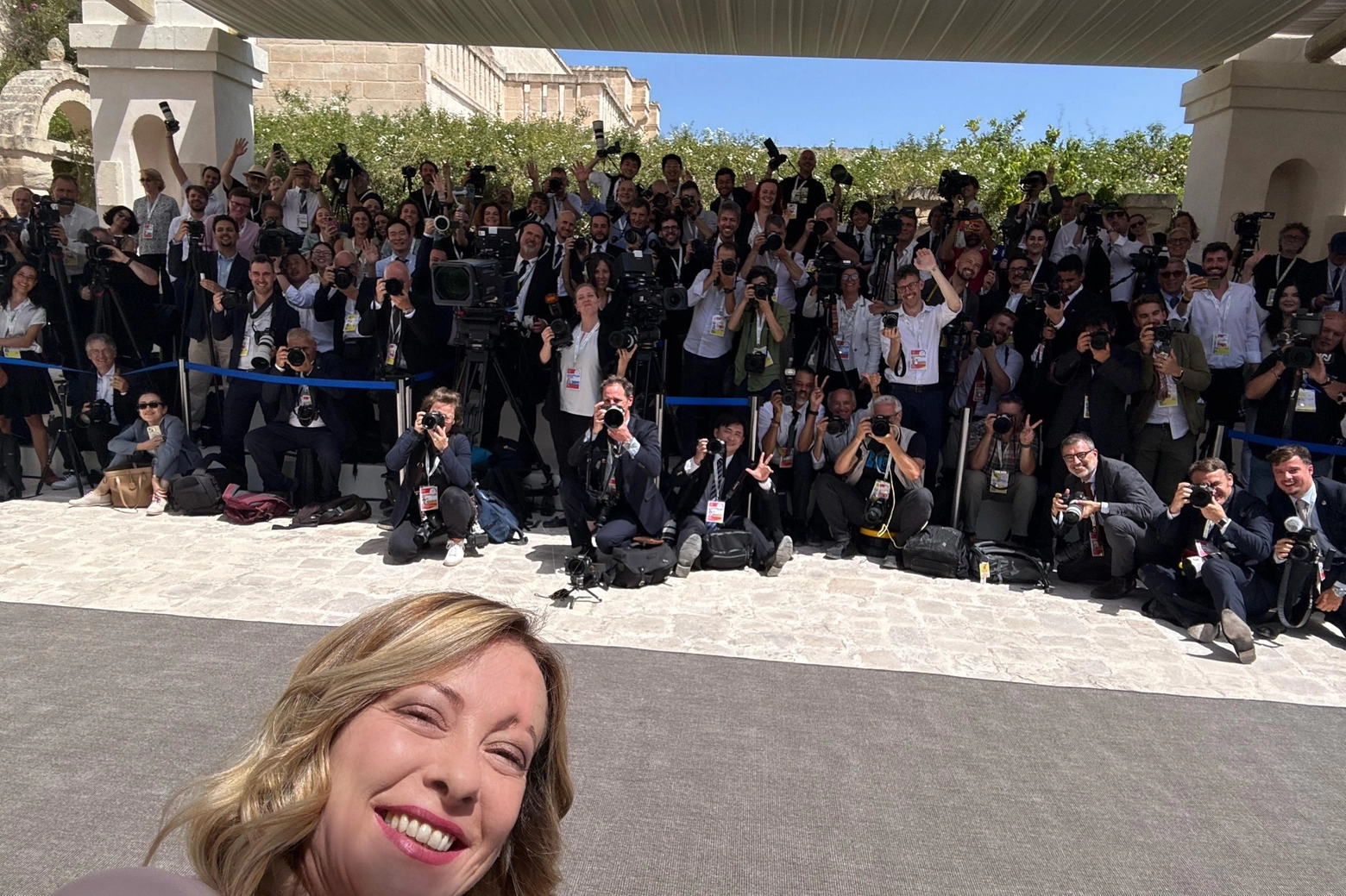La presidente del Consiglio Giorgia Meloni si fa un selfie con i fotografi ed i videomaker aprendo i lavori del G7 (Ansa)