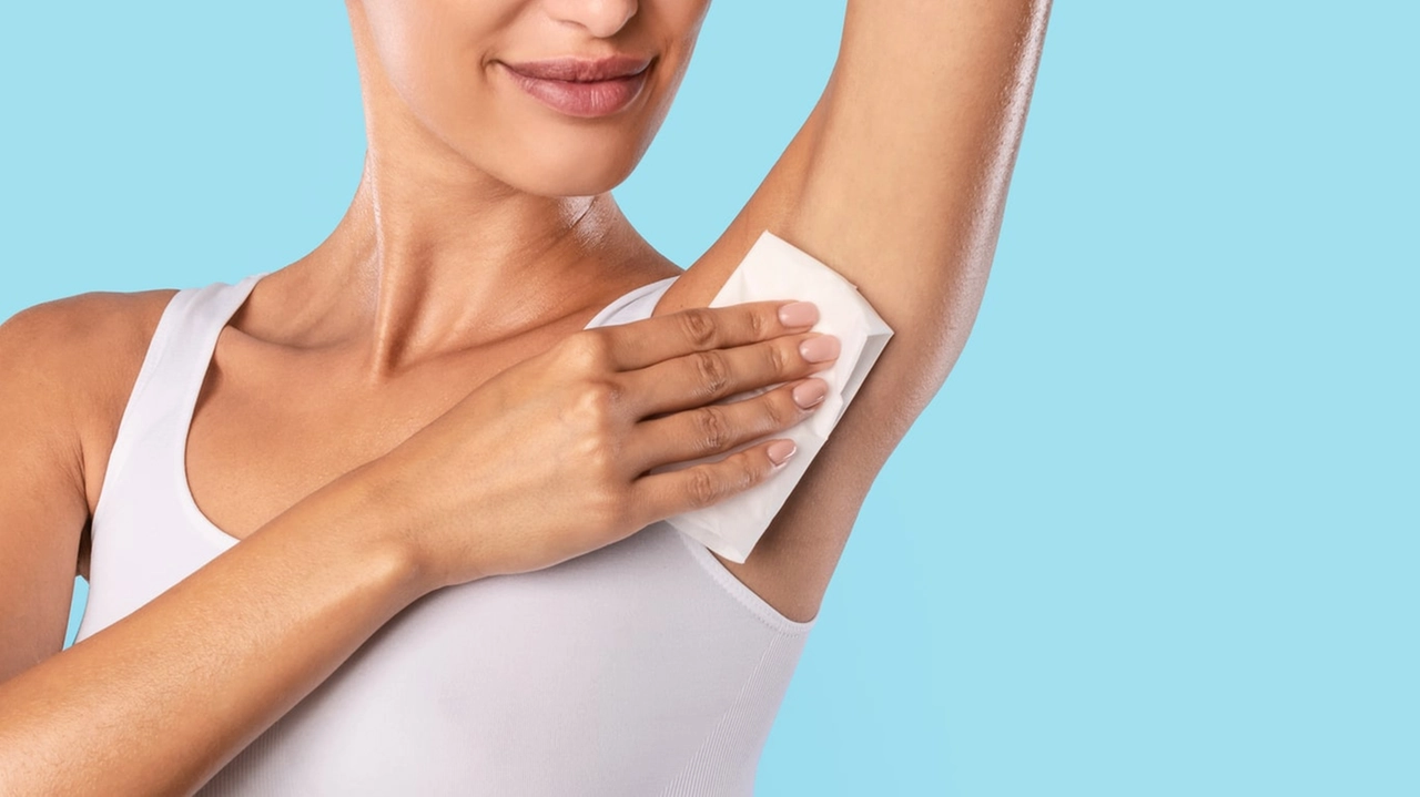 Hyperhidrosis Concept. Closeup cropped view of young lady wiping her under arm area with napkin towel, rubbing armpit isolated on blue studuo background, putting hand up, touching axilla. Perspiration