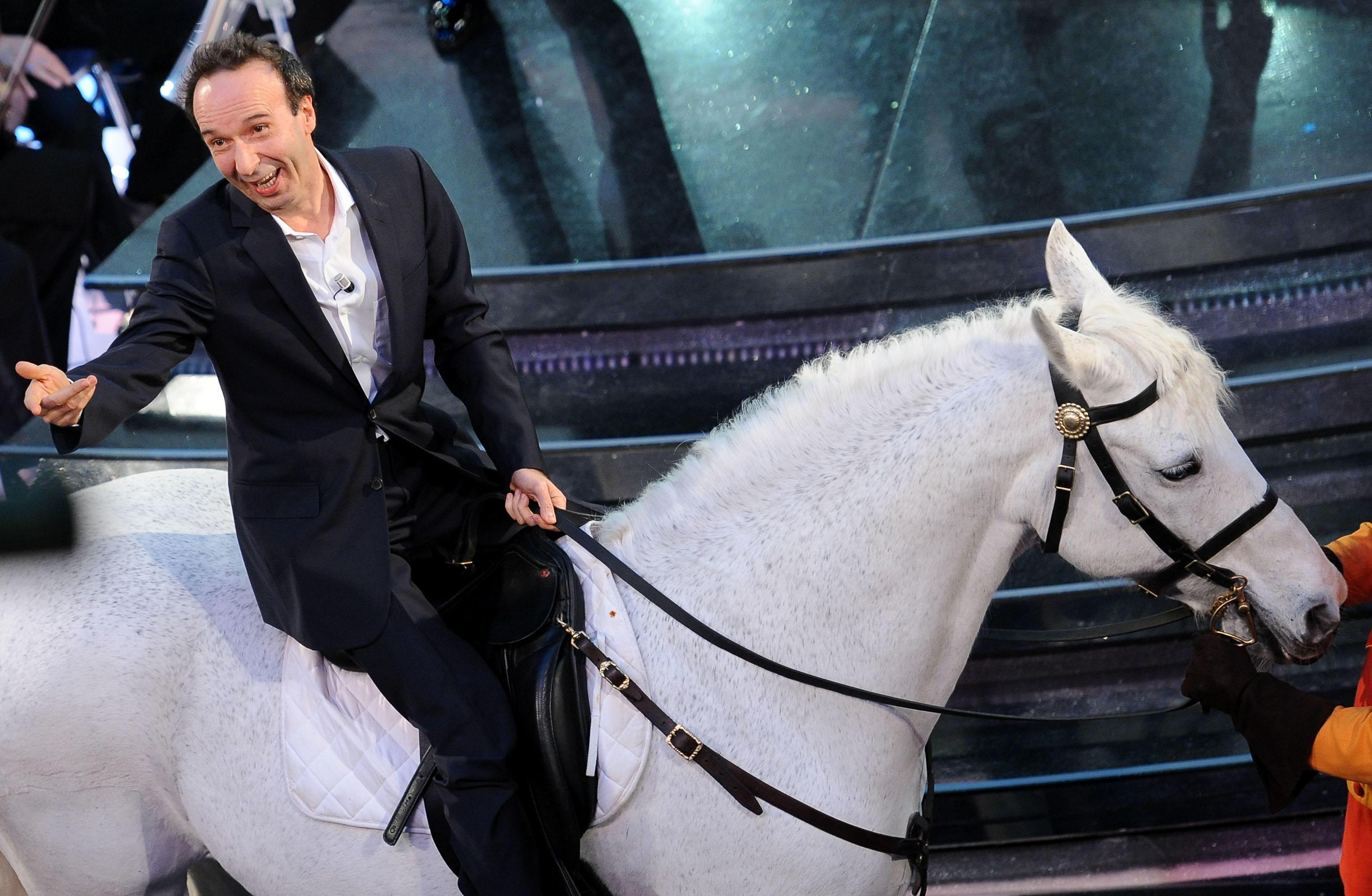 Benigni a Sanremo 2025 senza cachet. Le sei volte di Roberto all’Ariston: dalla ‘strizzata’ a Pippo Baudo all’entrata a cavallo