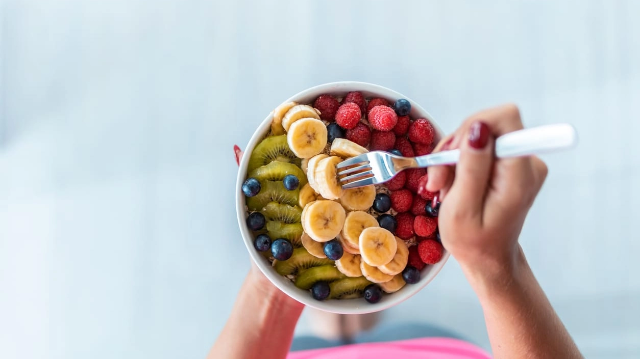 Woman's hands holding a bowl with fresh fruit while standing at home.