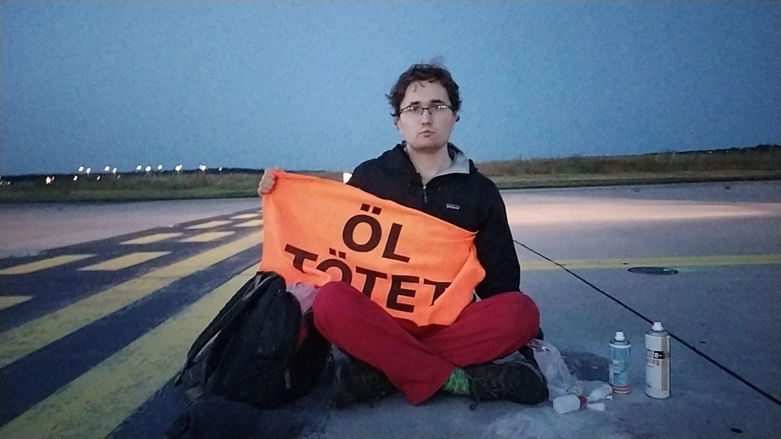 Un militante di Ultima Generazione seduto sulla pista dell'aeroporto di Francoforte