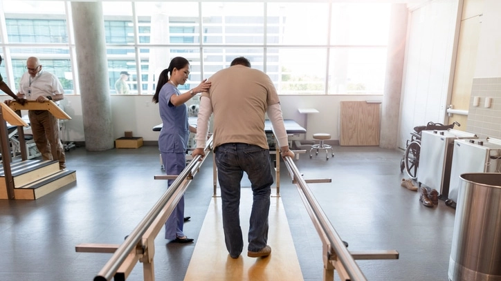 Man uses parallel bars in rehab center