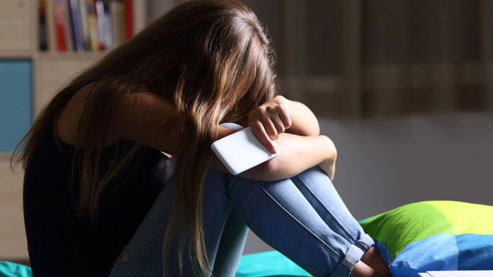 Sad teen with a phone in her bedroom