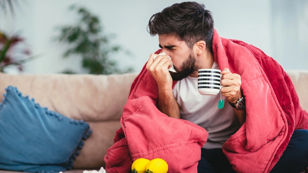 Man blowing his nose while lying sick in bed