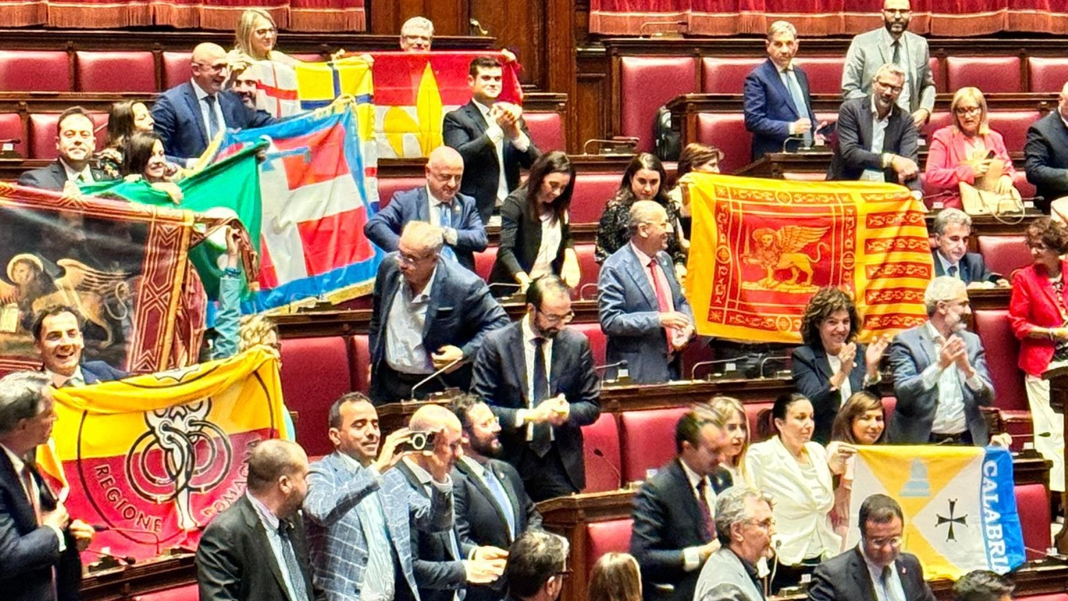 Bandiere locali in aula tra i banchi della maggioranza per festeggiare l'ok al ddl Autonomia alla Camera (Ansa)