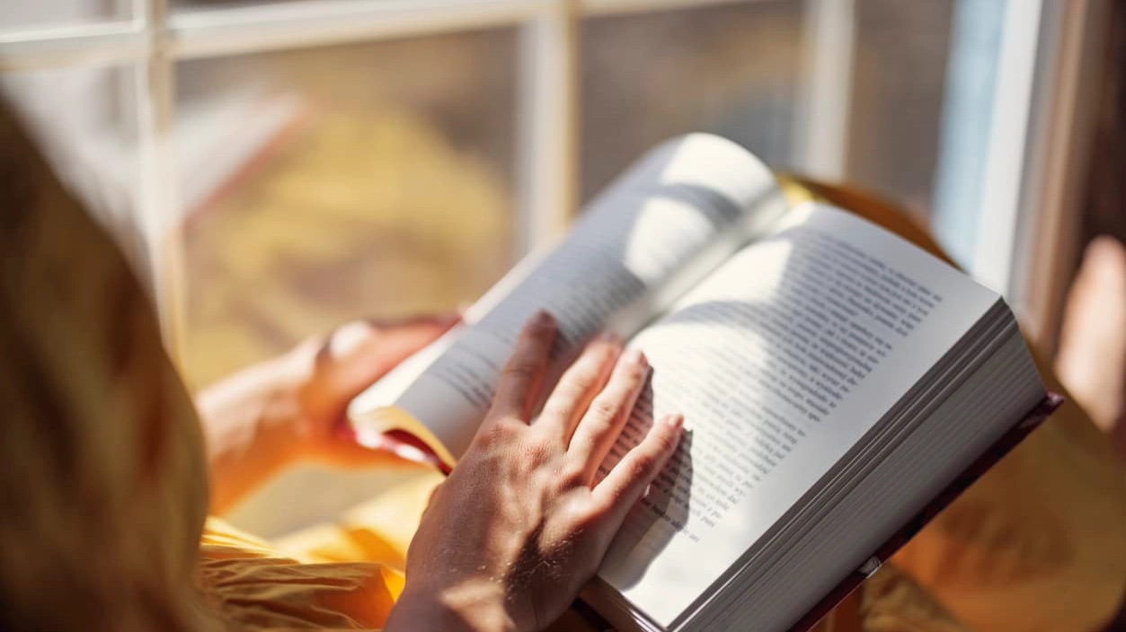 Teenage girl sitting on windowsill and reading a book