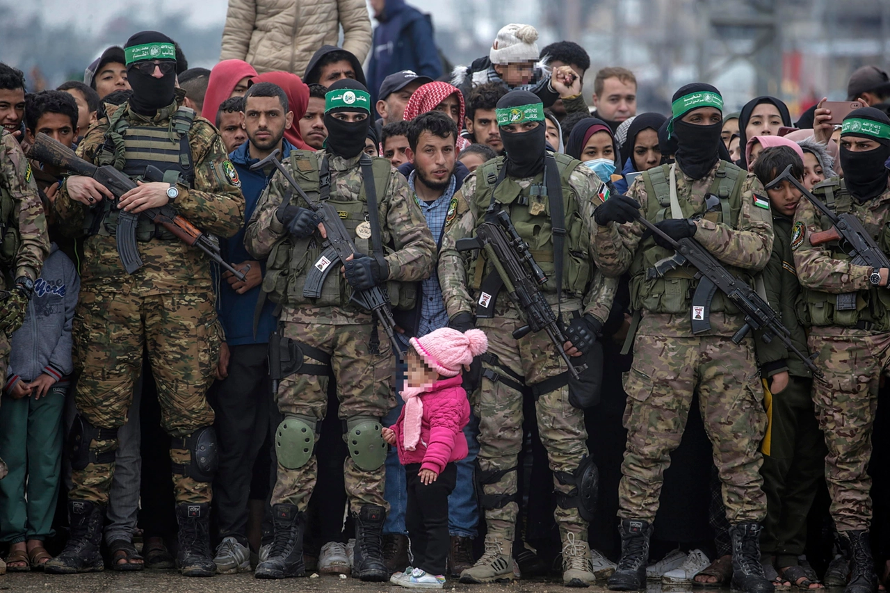 Bambina palestinese davanti a una milizia armata di Hamas (Ansa)